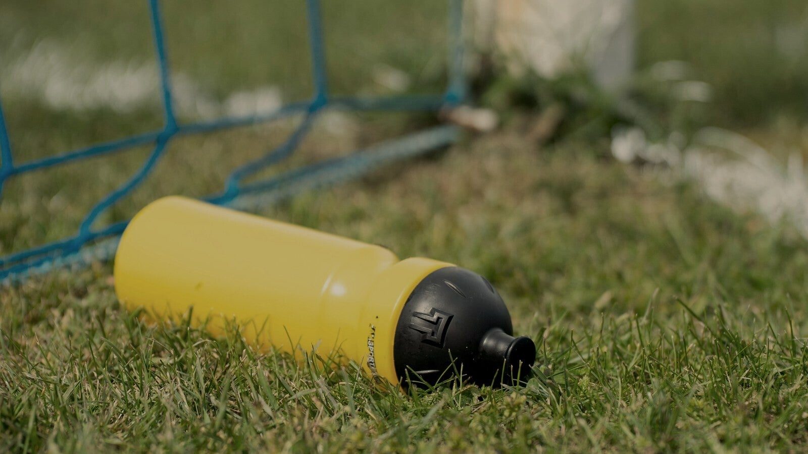 Yellow water bottle in the grass by a football goal, hydration for young footballers