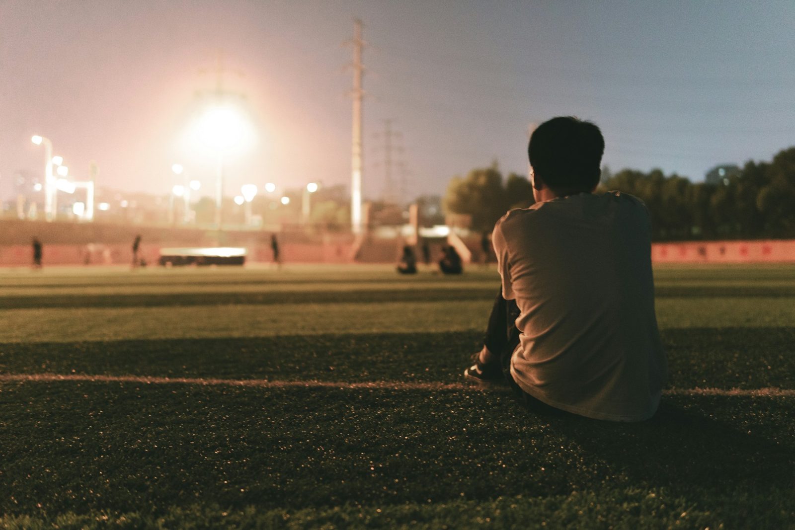 Player sitting at the side of the pitch before evening training under the floodlights