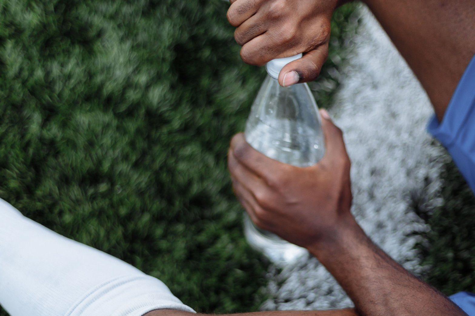 Footballer sitting on the pitch with a water bottle after exertion, the start of post-match recovery